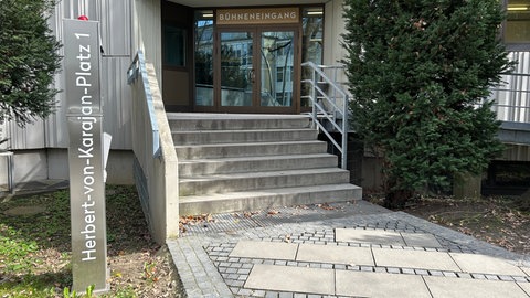 Eine Stele mit der Adresse "Herbert-von-Karajan-Platz 1" vor dem Bühneneingang des Theaters Ulm als Zeichen des Gedenkens an Karajan.