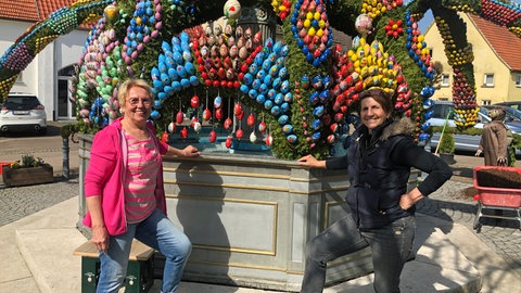 Iris Jekel (re.) und Marianne Kolb (li.). Rund 13.500 Eier schmücken den Osterbrunnen Schechingen im Jahr 2026.