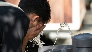 Junge kühlt sich an einem Wasserspender ab.