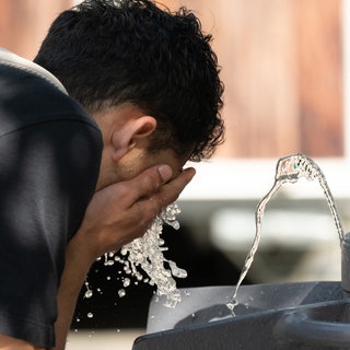 Junge kühlt sich an einem Wasserspender ab.
