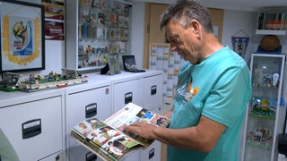Peter Saß blättert in einem seiner rund 1.000 Alben mit Fotos von Fußballspielern.
