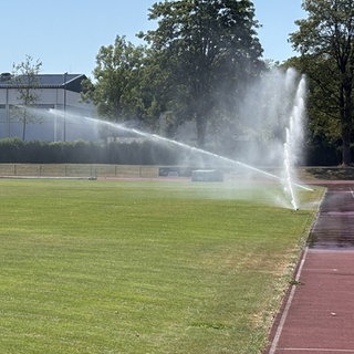 Ein Sportplatz, auf dem zwei Rasensprenger laufen. Die Stadt Neu-Ulm bewässert bei großer Hitze ihre Sportplätze täglich und stundenlang.