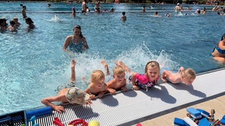 Mehrere Kinder halten sich am Beckenrand fest. Beim Schwimm-Crashkurs sollen die Schülerinnen und Schüler schnell lernen, sich allein über Wasser zu halten.