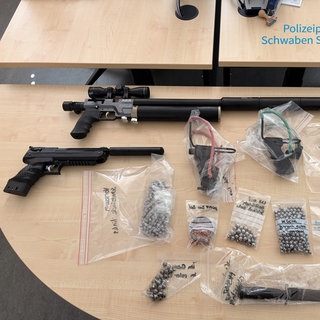 Mehrere Waffen und Stahlkugeln liegen auf einem Tisch. Die Steinschleudern, Luftdruckwaffen und anderen Gegenstände wurden von der Polizei bei einem 66-jährigen Tatverdächtigen aus Senden-Ay gefunden.