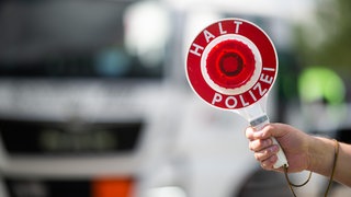 Ein Polizist hält eine Polizeikelle (Symbolbild).  Bei einer Verkehrskontrolle nahe Ulm haben Polizisten einen Lastwagenfahrer erwischt, der seine Lenkzeiten massiv überschritten hat.