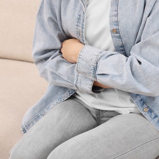 Eine Frau sitzt auf einem Sofa und hält sich den Magen. Nach zahlreichen Magen-Darm-Erkrankungen nach einem Landfrauenfest steht das Norovirus als Ursache fest.