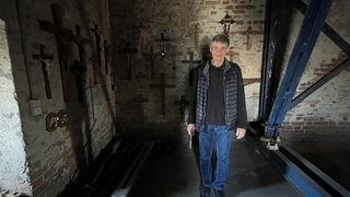 Kreuze hängen an einer alten Wand in einem Kirchturm: In der Georgskirche bekommen alte Kreuze und Kruzifixe eine neue Heimat
