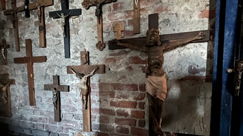Kreuze hängen an einer alten Wand in einem Kirchturm: In der Georgskirche bekommen alte Kreuze und Kruzifixe eine neue Heimat