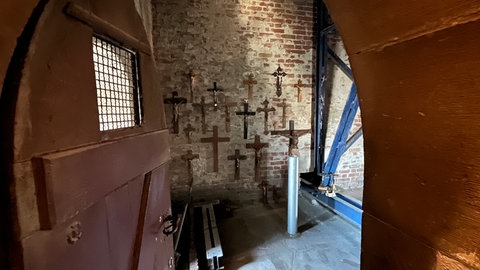 Kreuze hängen an einer alten Wand in einem Kirchturm: In der Georgskirche bekommen alte Kreuze und Kruzifixe eine neue Heimat