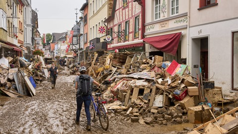 Eine Frau schiebt ihr Fahrrad durch den Schlamm. Anwohner und Ladeninhaber versuchen, ihre Häuser vom Schlamm zu befreien und unbrauchbares Mobiliar nach draußen zu bringen.