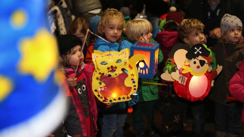Kinder halten ihre bunten, selbstgebastelten Laternen bei einem Martinsumzug fest.