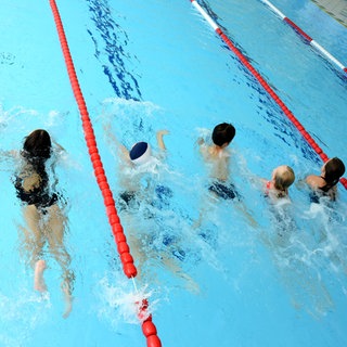 Schülerinnen und Schüler nehmen in einem Hallenbad am Schwimmunterricht teil. 