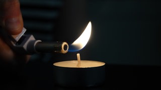Eine Kerze wird mit einem Feuerzeug angezündet - für den Fall eines Blackouts sollten in jedem Haushalt Kerzen und Streichhölzer vorhanden sein.