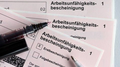 Stifte liegen auf den Arbeitsunfähigkeitsbescheinigungen für Arbeitnehmer im Falle einer Krankschreibung durch den Arzt.