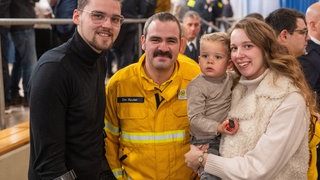 Feuerwehrmann Christoph Reuter (M) steht mit Mark Visser (l), Edi Hoefnagel-Visser und Sohn Jamie beim Neujahrsempfang der Gemeinde Kröv. Reuter war an der Rettung der Familie beteiligt, die im August 2024 beim Einsturz eines Hotel an der Mosel verschüttet wurde.