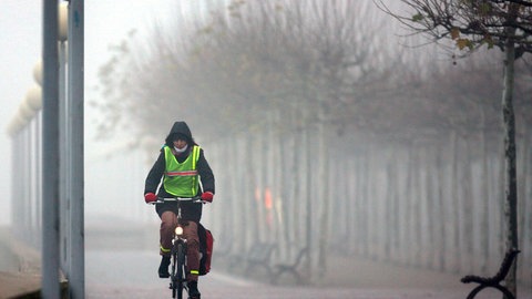 Eine Fahrradfahrerin radelt im Nebel. 