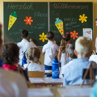 Schüler im Klassenzimmer vor einer Schultafel, auf die sie ihre Namen schreiben. 
