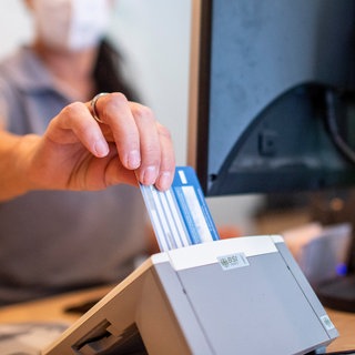 Die Hausarztpraxen in RLP sind überlastet - eine Medizinische Fachangestellte schiebt in einer Hausarztpraxis die Versichertenkarte der Krankenkasse eines Patienten in das Lesegerät. 