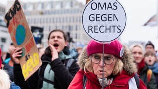 Eine ältere Frau mit pinker Mütze hält bei einer Demo gegen den Fall der Brandmauer zur AfD ein Schild mit der Aufschrift "Omas gegen rechts" hoch.