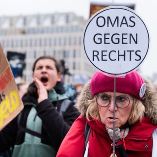 Eine ältere Frau mit pinker Mütze hält bei einer Demo gegen den Fall der Brandmauer zur AfD ein Schild mit der Aufschrift "Omas gegen rechts" hoch.