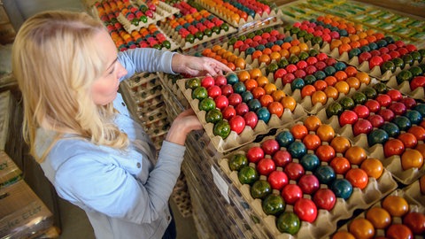 Eine Frau steht vor Paletten mit bunten Ostereiern. Trotz hoher Nachfrage gibt es keinen Engpass vor Ostern