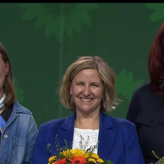 Drei Frauen der Partei Die Grünen mit Blumensträußen auf der Bühne