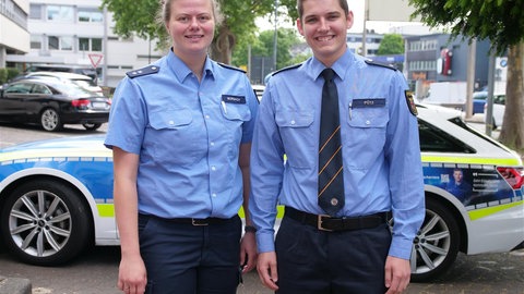 Joanna Morbach und David Pütz, Polizisten im Präsidium Koblenz, stehen vor einem Streifenwagen.
