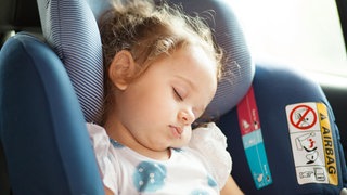 Ein schlafendes Baby in einer Babyschale im Auto. Bei Hitze sollten Kinder auf keinen Fall alleine im Auto gelassen werden. Lebensgefahr.