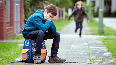 Ein Junge sitzt nach der Zeugnisausgabe traurig auf seiner Schultasche (Symbolbild).