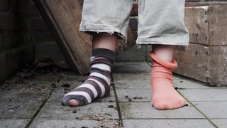 Kinderarmut: ein Kind mit zwei unterschiedlichen Socken, ein geringelter Strumpf ist kaputt.