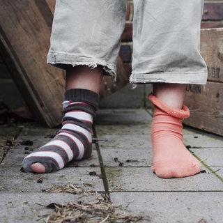 Kinderarmut: ein Kind mit zwei unterschiedlichen Socken, ein geringelter Strumpf ist kaputt.