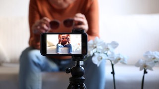 Ein Influencer filmt sich selbst auf der Couch mit seinem Smartphone auf einem Stativ. Das Finanzamt prüft jetzt, ob Influencer wie er ihre Steuern korrekt abgeführt haben.
