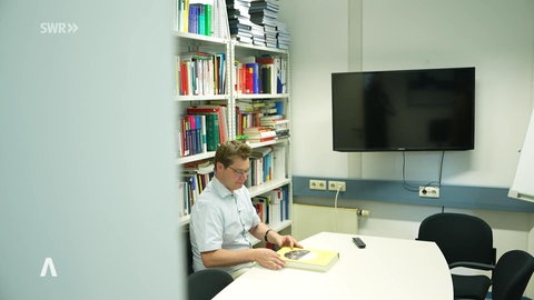 Männliche Person mit einem gelben Buch in einem Büro mit Buchregal