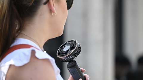 Eine junge Frau nutzt einen tragbaren Ventilator, um sich von der Hitze abzukühlen. In Rheinland-Pfalz könnte es diese Woche bis zu 38 Grad heiß werden.