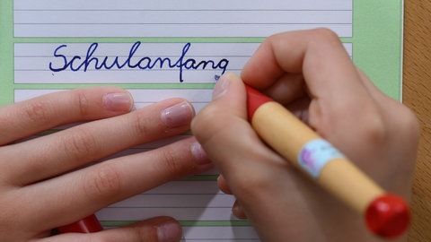 Eine Person schreibt "Schulanfang" in ein Heft.