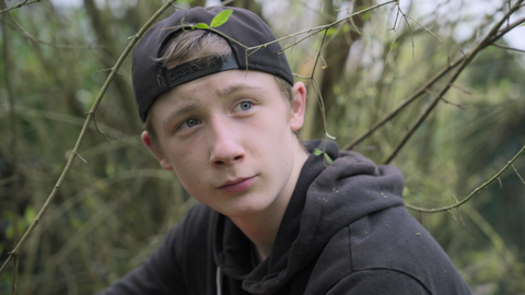 Gabriel mit einer Basecap vor einem Busch