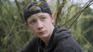 Gabriel mit einer Basecap vor einem Busch