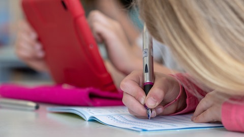 Ein Mädchen schreibt mit einem Füller in ein Schulheft: Das neue Schuljahr hat in RLP begonnen, eine Neuerung ist: Es gibt keine unangkündigten Überprüfungen der Hausaufgaben mehr. (Symbolbild: Schülerin schreibt in ihr Heft)