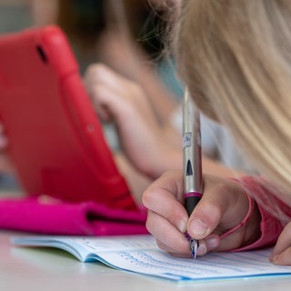Ein Mädchen schreibt mit einem Füller in ein Schulheft: Das neue Schuljahr hat in RLP begonnen, eine Neuerung ist: Es gibt keine unangkündigten Überprüfungen der Hausaufgaben mehr. (Symbolbild: Schülerin schreibt in ihr Heft)