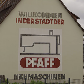 Auf einem Haus ist ein Werbeblock mit der Aufschrift: Willkommen in der Stadt der Pfaff Nähmaschinen