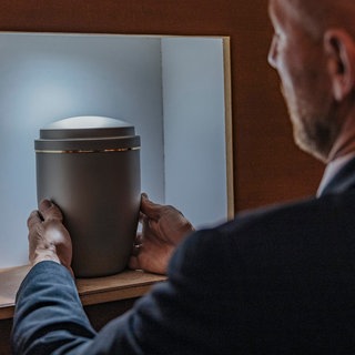 Ein Mann stellt eine Urne in ein Regal. 