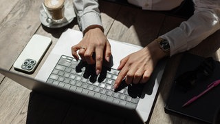 Junge Frau tippt auf einem Laptop an einem Cafétisch: Bei der Mainzer und Wormser Gründungswoche bekommen Interessierte ab dem 17. November einen ersten Einblick in Gründungsthemen.