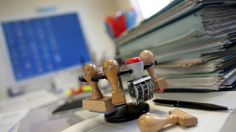 Schreibtisch in einer Behörde mit Stempeln und Akten (Symbolbild): Laut Rechnungshof haben zwei Kommunen insgesamt fünf Beschäftigte rechtswidrig über Jahre hinweg bei voller Bezahlung von der Arbeit freigestellt.