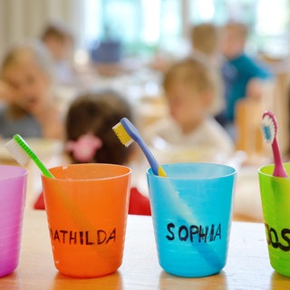 Bunte Zahnputzbecher in einer Kita. In Rheinland-Pfalz fehlen fast 20.000 Plätze in Kindertagesstätten.