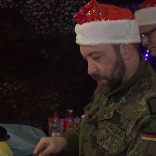 Zwei Soldaten tragen eine Weihnachtsmütze und bedienen Gäste auf einem Weihnachtsmarkt