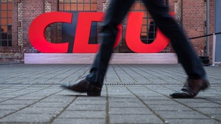 Ein Mann läuft an einem CDU-Partei-Logo vorbei. Die CDU RLP verklagt die Landesregierung auf Auskunftspflicht.