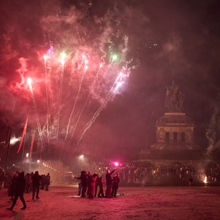 Menschen feiern vor der Reiterstatue am Deutschen Eck in Koblenz Silvester.
