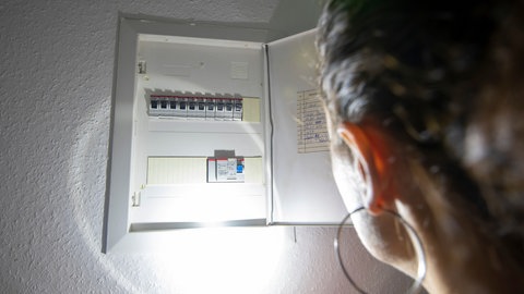 Eine Frau leuchtet mit einer Taschenlampe in einen Sicherungskasten - In RLP gilt bei einem Blackout Eigenvorsorge