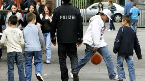 Ein Polizist zwischen Schülerinnen und Schülern auf einem Schulhof - Mehr Präsenz soll die Sicherheit stärken (Archivbild)