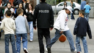 Ein Polizist zwischen Schülerinnen und Schülern auf einem Schulhof - Mehr Präsenz soll die Sicherheit stärken (Archivbild)